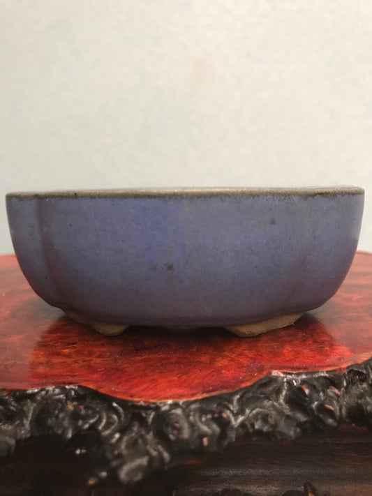 A small, deep blue glazed ceramic pot with a matte finish rests on a red wooden stand.