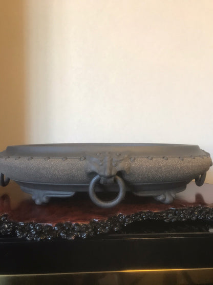 Dark grey, matte-finished ceramic pot with a central ring handle and rivet-like details.