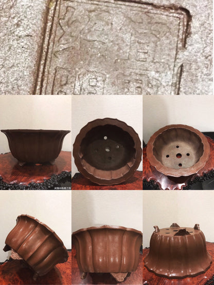 A dark brown, fluted ceramic pot with three feet and drainage holes, showing an engraved mark on its base.