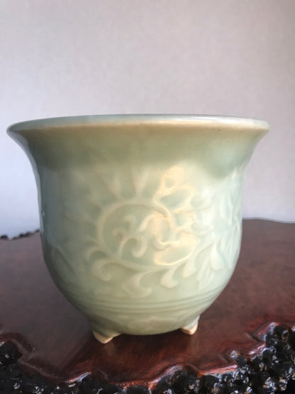 A pale green glazed ceramic pot with raised floral pattern and three feet.