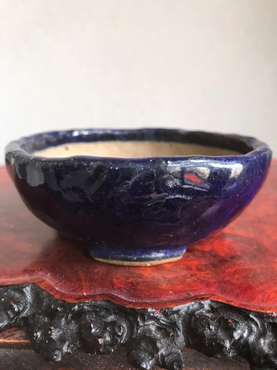 A glossy dark blue ceramic pot with a rough rim sits on a red wooden stand.