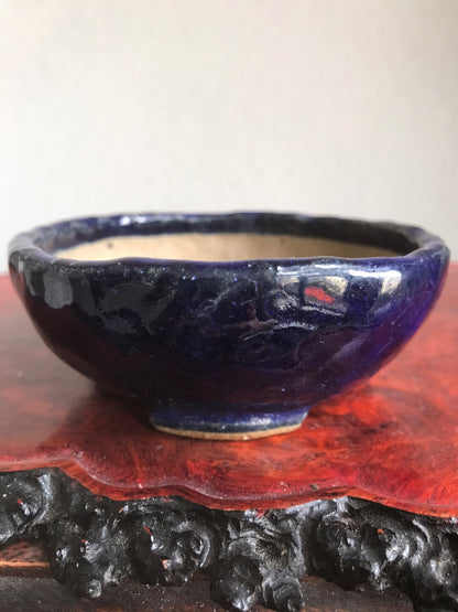 A glossy dark blue ceramic pot with a rough rim sits on a red wooden stand.