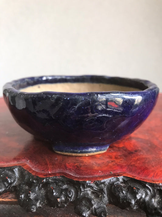 A glossy dark blue ceramic pot with a rough rim sits on a red wooden stand.