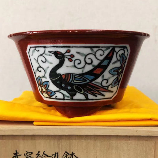 Three glazed ceramic pots with red rims, white interiors, and black dragon motifs on a yellow cloth.