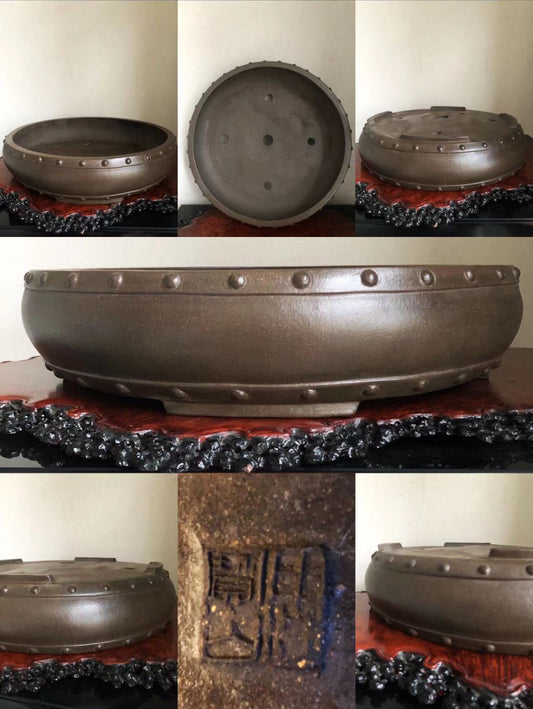 Dark brown glazed pot with rivet-like bumps around rim and a stamped mark on base.