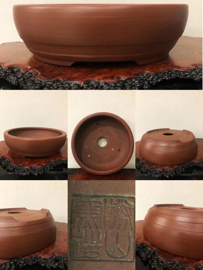 A reddish-brown unglazed ceramic pot with a wide rim, three drainage holes, and a square maker’s mark.