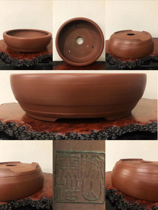 A reddish-brown unglazed ceramic pot with a wide rim, three drainage holes, and a square maker’s mark.
