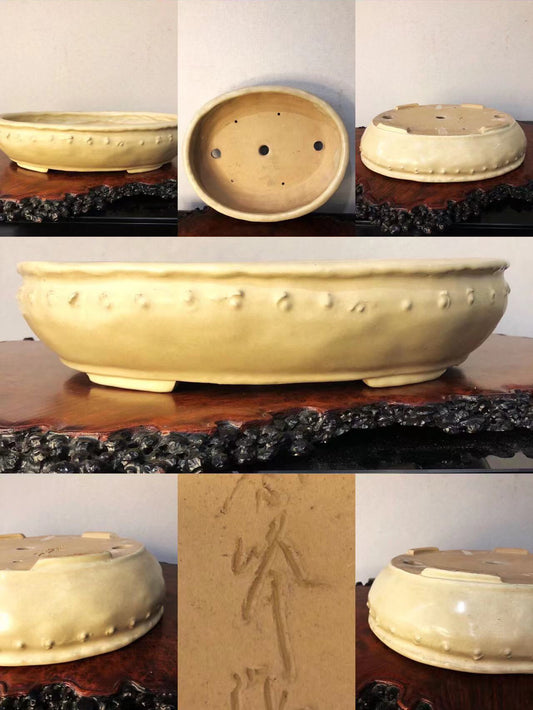 A pale yellow glazed ceramic pot with raised dots and carved characters on its base.