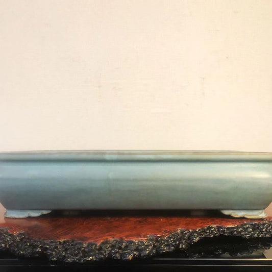 A light blue glazed rectangular pot with four feet and an engraved mark on its base.