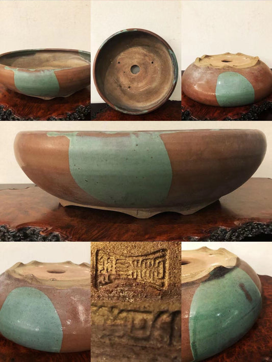 A round ceramic pot with brown and green glazed sections and a stamped mark on its base.