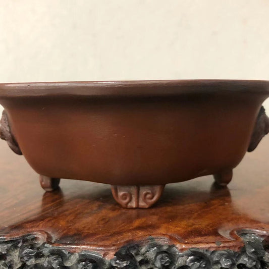 Dark brown glazed ceramic pot with lion-head handles and carved feet, showing interior and base markings.