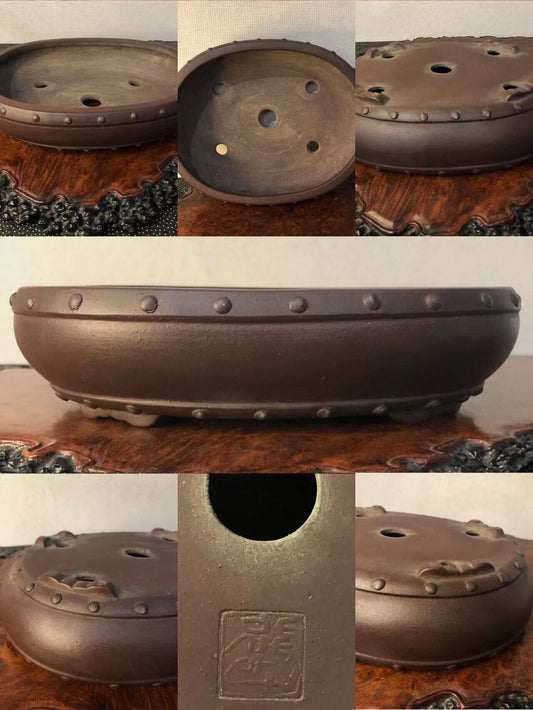 Dark brown glazed pot with rivet-like bumps around rim and three drainage holes on base.