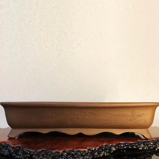 A long, shallow, brown glazed pot with carved characters and a square base with a central hole.