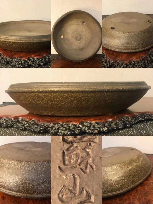 A dark, speckled glazed pot with three drainage holes and carved characters on its base.