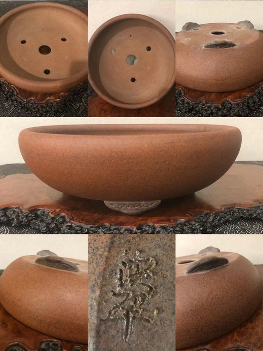 A round, brown, unglazed ceramic pot with three drainage holes and an incised signature.