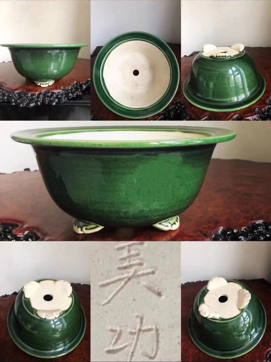 Dark green glazed pot with white floral decoration and three feet, showing interior and base markings.