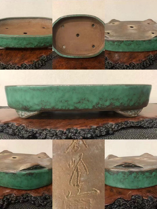 A green glazed pot with a brown interior, four drainage holes, and an engraved mark on its base.