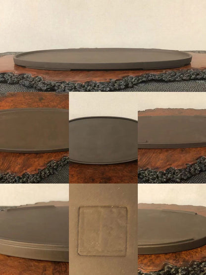 A dark grey, oval-shaped, unglazed ceramic bonsai pot with a square maker’s mark.