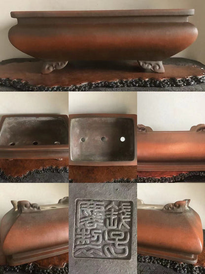 A dark brown, glossy, rectangular bonsai pot with three holes and carved feet, featuring a square seal with characters.