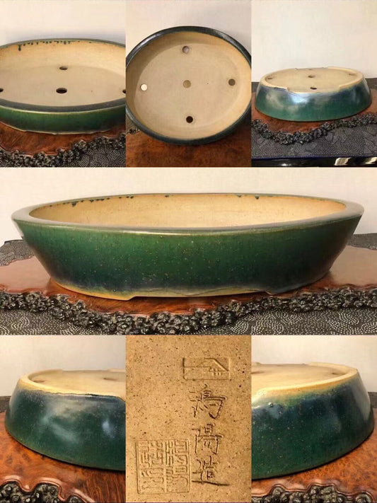 Oval glazed pot, dark green outside, beige inside, with three drainage holes and a maker's mark.
