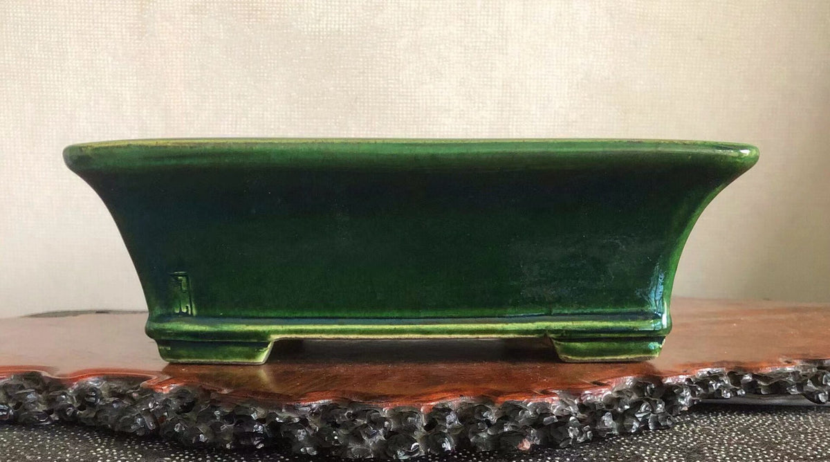 A glossy, deep green rectangular ceramic pot with slightly curved sides and a small mark on its left side.