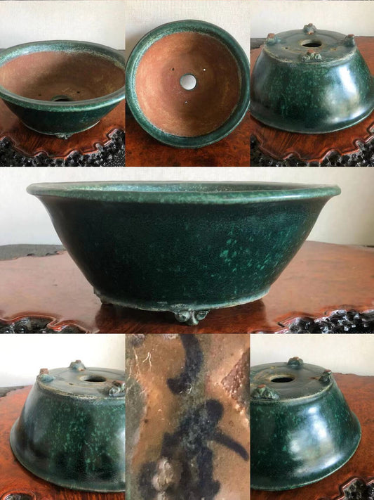 Dark green glazed pot with three feet, showing interior and base markings.