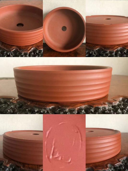 A terracotta bonsai pot with horizontal ridges and a central drainage hole.