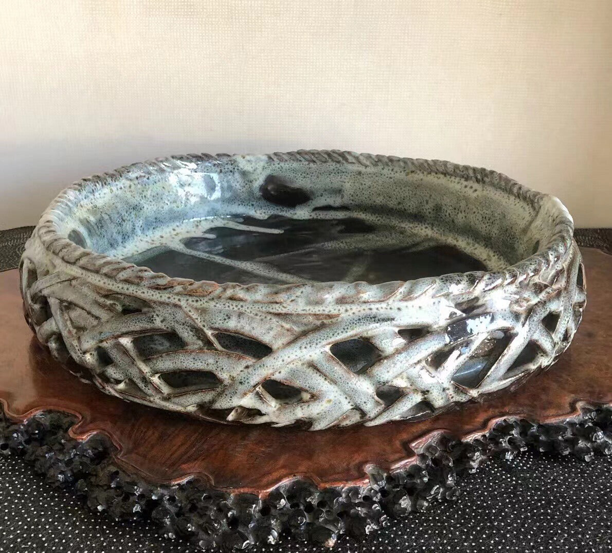 A wide, shallow ceramic bowl with a speckled grey glaze and intricate woven pattern around its rim.