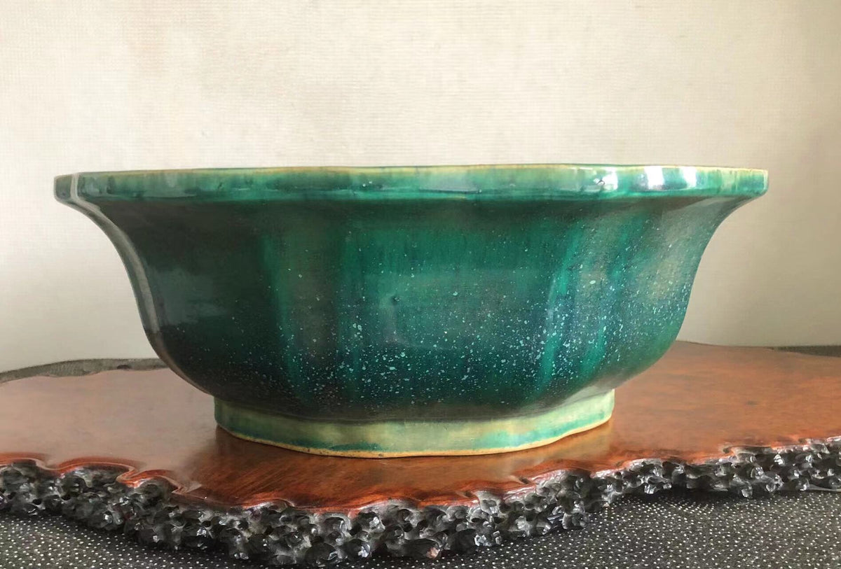 A wide, glossy green glazed ceramic pot with flared sides rests on a wooden stand.