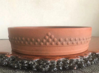 A terracotta bonsai pot with a matte finish and a decorative band of raised dots around its rim.