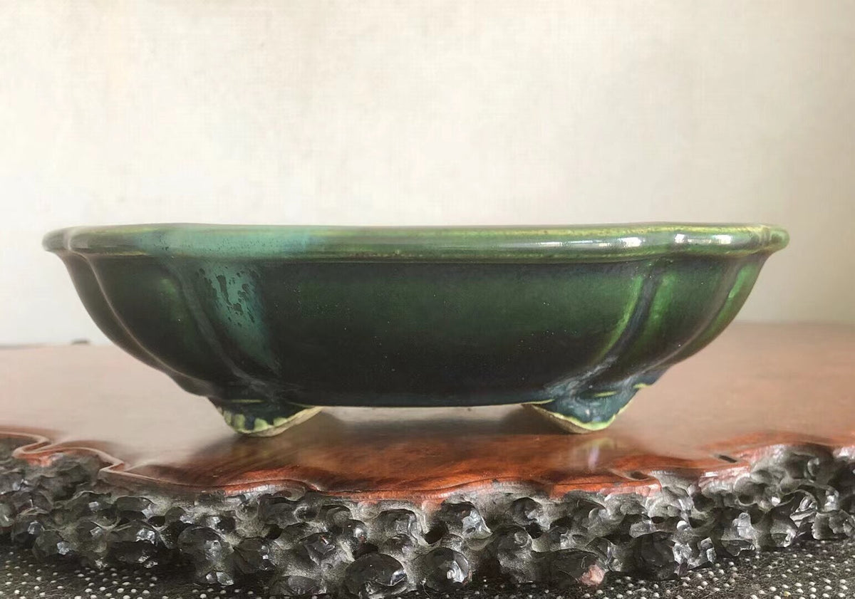 A glossy green glazed ceramic pot with three feet, shallow bowl shape.