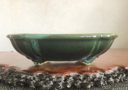A glossy green glazed ceramic pot with three feet, shallow bowl shape.
