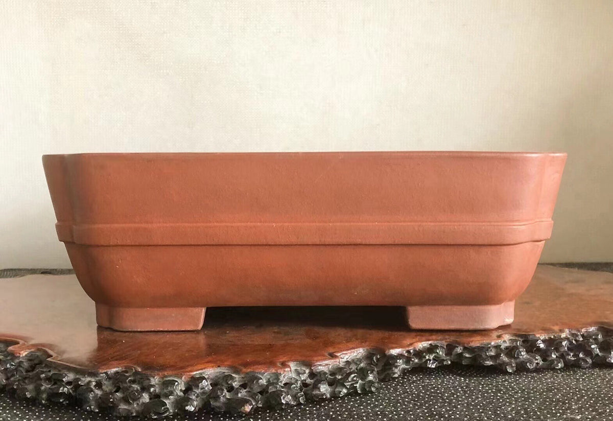 Square terracotta pot with matte finish and two horizontal ridges, resting on four short feet.