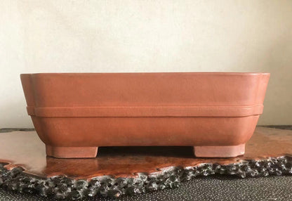 Square terracotta pot with matte finish and two horizontal ridges, resting on four short feet.