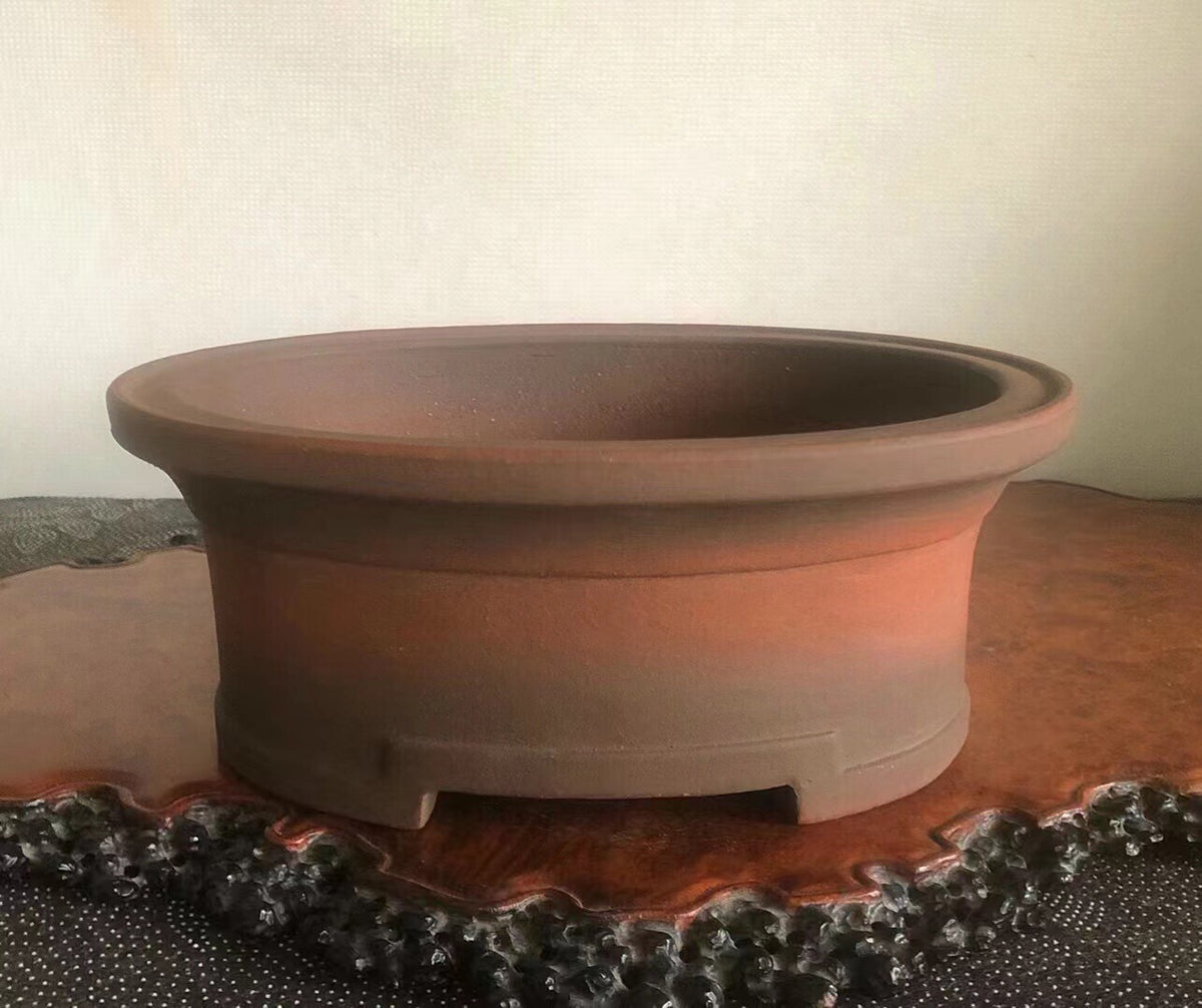 A round, unglazed terracotta bonsai pot with a wide rim and footed base.