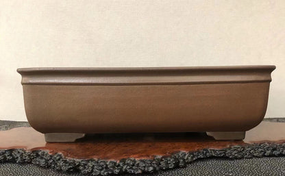 A matte brown rectangular pot with rounded corners and four small feet rests on a wooden display stand.