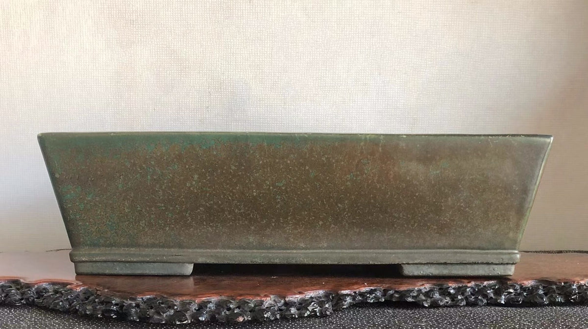 Rectangular glazed pot with mottled green and brown patina, resting on a dark stone slab.