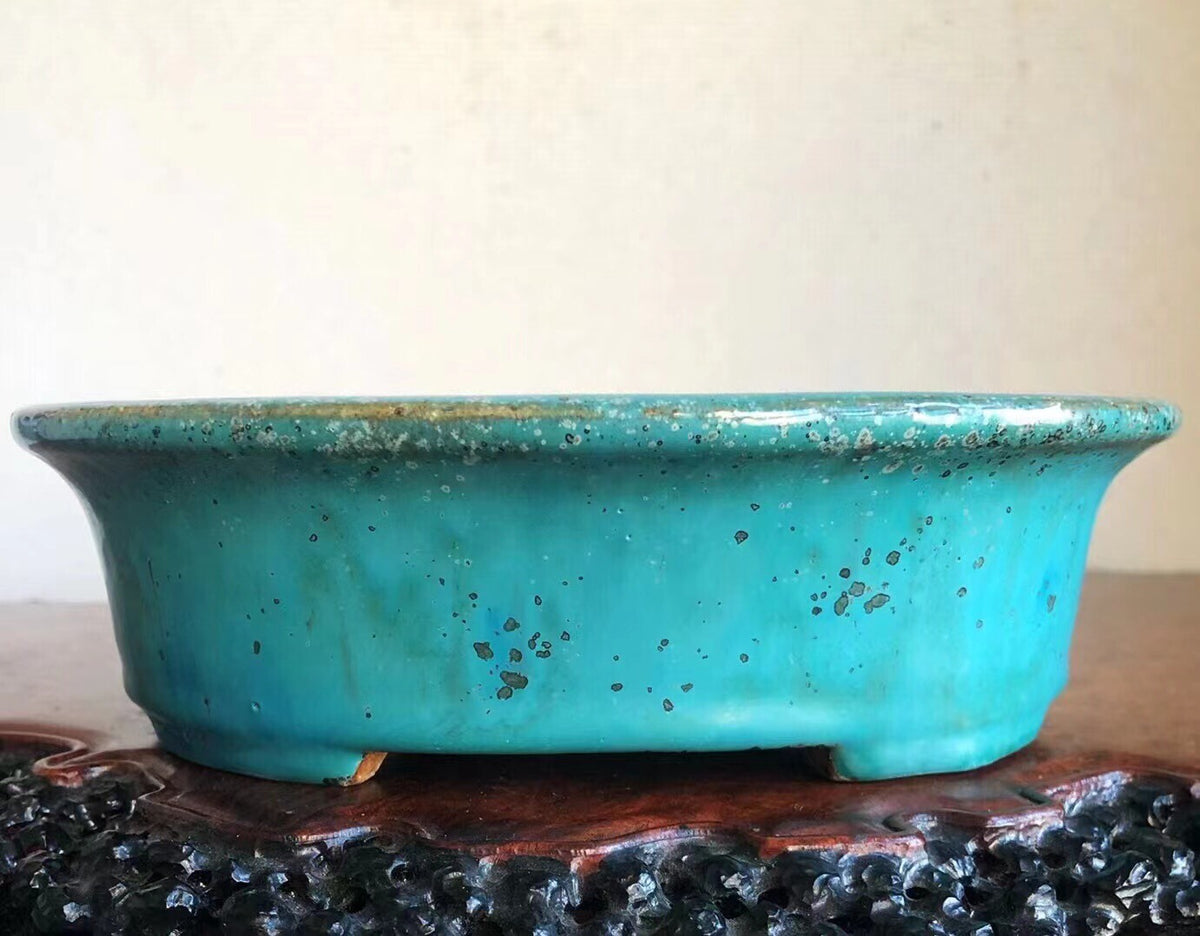 A turquoise glazed pot with speckles and a worn rim sits on a dark wooden stand.