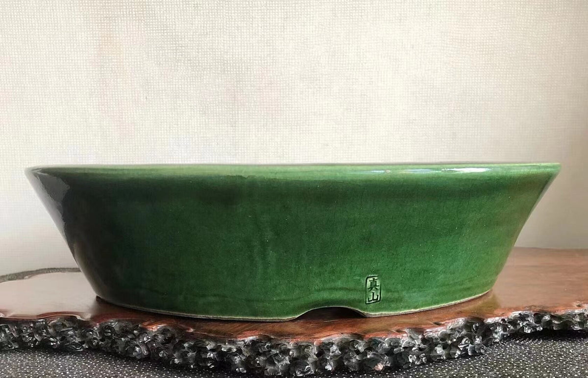 A glossy green glazed ceramic pot with a small square mark on its side.