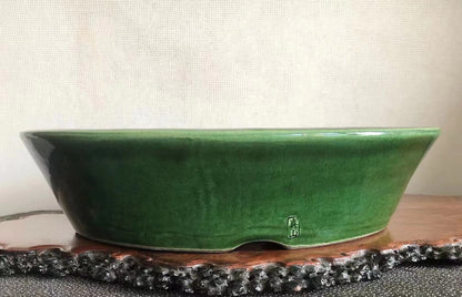 A glossy green glazed ceramic pot with a small square mark on its side.
