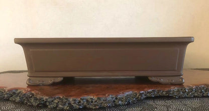 A matte brown rectangular pot with curved feet rests on a wooden base.