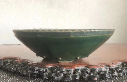 Dark green glazed ceramic bowl with scalloped rim, resting on a textured wooden base.