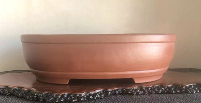 A terracotta bonsai pot with a smooth, unglazed surface and a wide, shallow bowl shape.