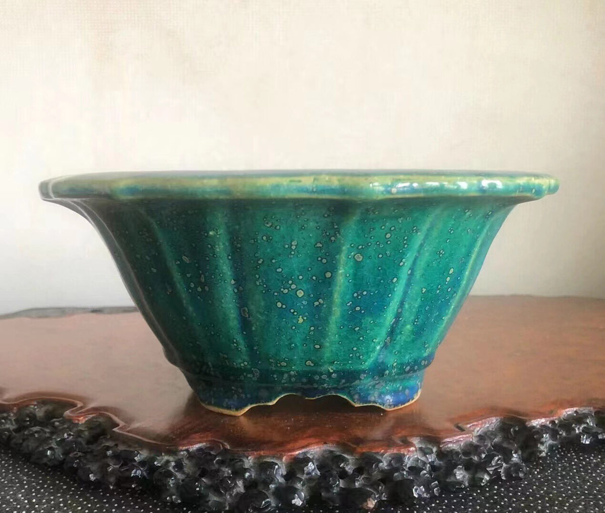 A glossy teal ceramic pot with fluted sides and speckled glaze sits on a wooden tray.