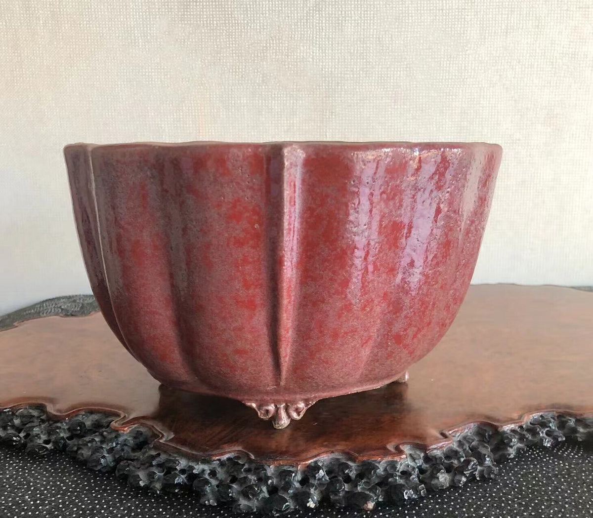 A glossy, deep red ceramic pot with fluted sides and three small feet.