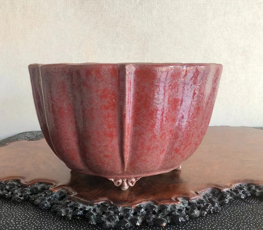 A glossy, deep red ceramic pot with fluted sides and three small feet.
