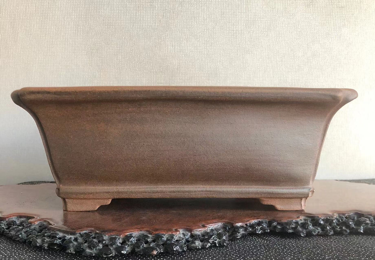 A matte brown rectangular pot with curved sides and a flat base rests on a wooden stand.