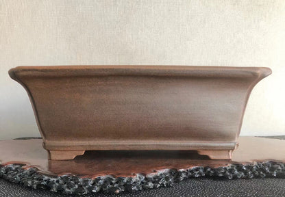 A matte brown rectangular pot with curved sides and a flat base rests on a wooden stand.