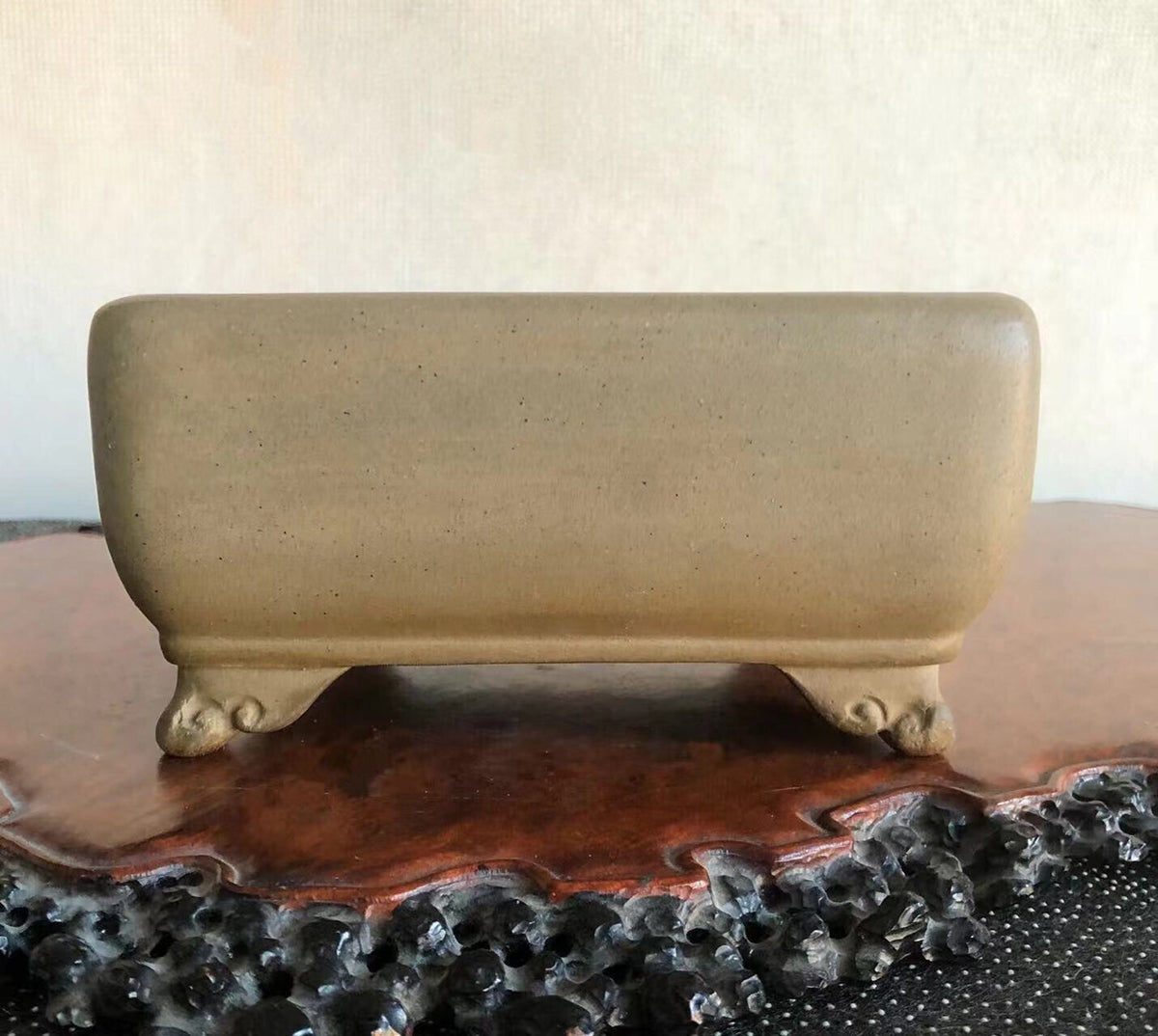 A beige, rectangular, unglazed ceramic pot with four carved feet rests on a wooden stand.