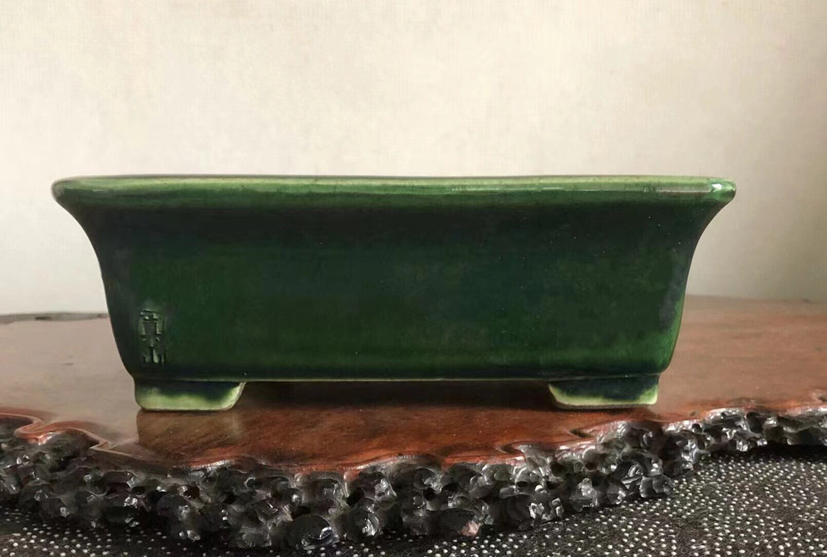 A glossy, dark green rectangular ceramic pot with a small mark on its side.